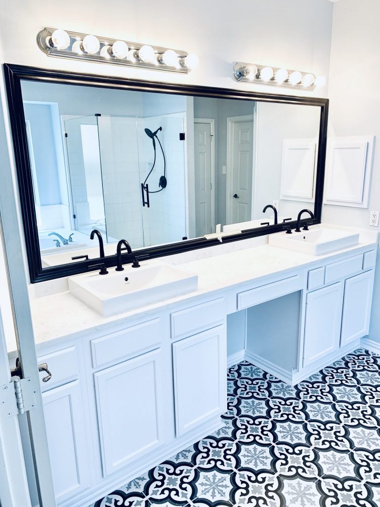 Black Frame around Master Bathroom Mirror with Black Faucets and White Quartz Countertops and White sinks and white cabinets